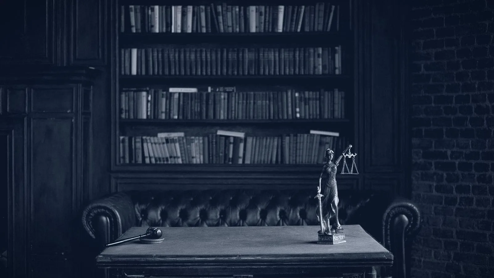 A dark wood library with a leather sofa and a small statue of Justice on the desk, printed in navy and white.