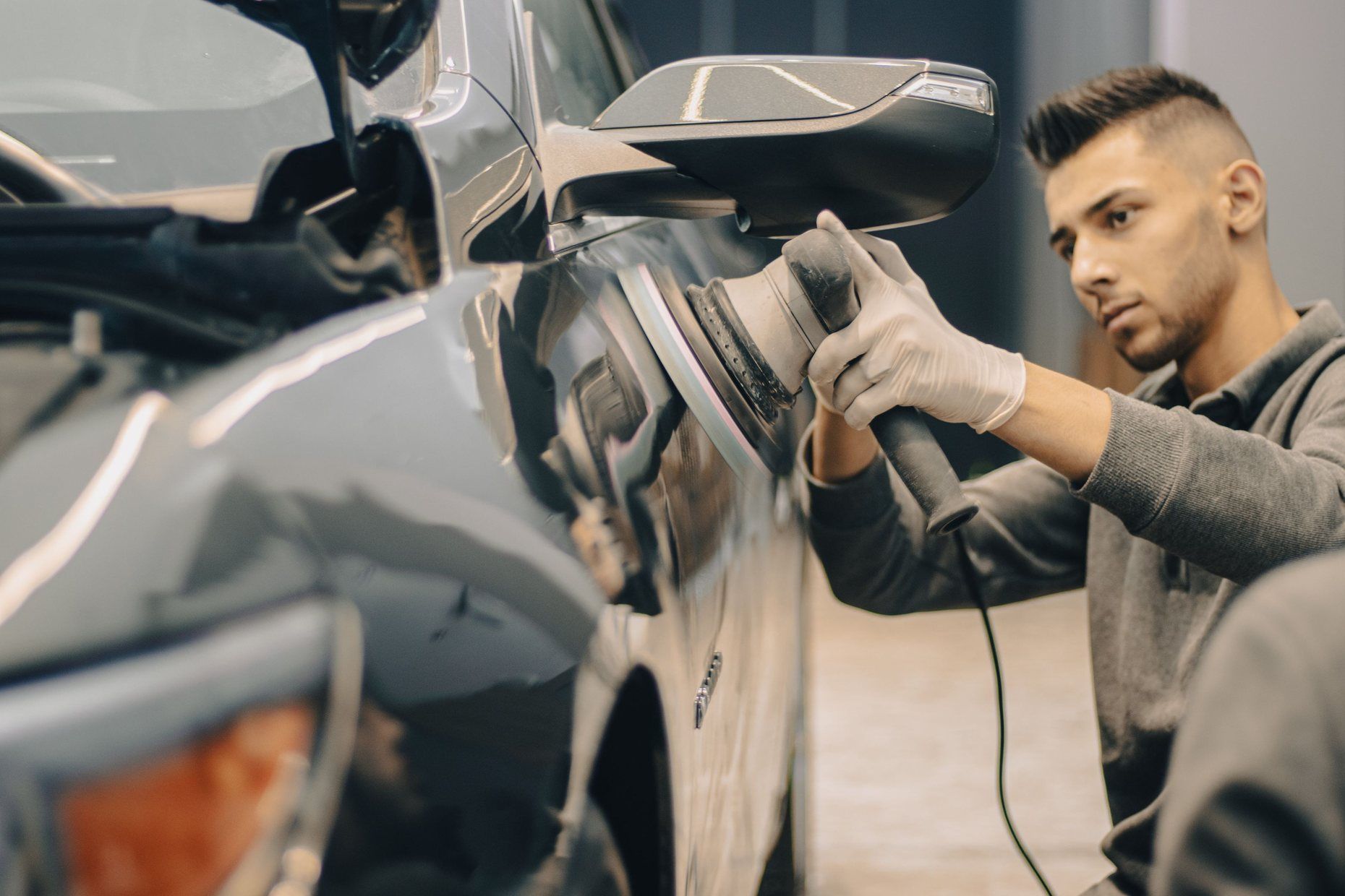 A body-shop worker polishing the repaired side panel of a silver car.