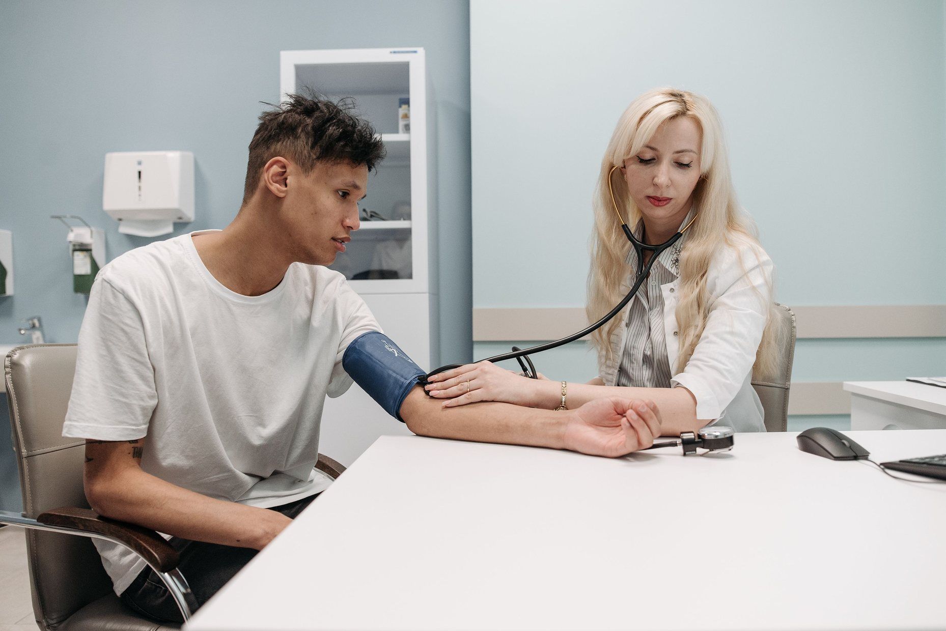 A doctor taking a young man’s blood pressure across a clinic desk.