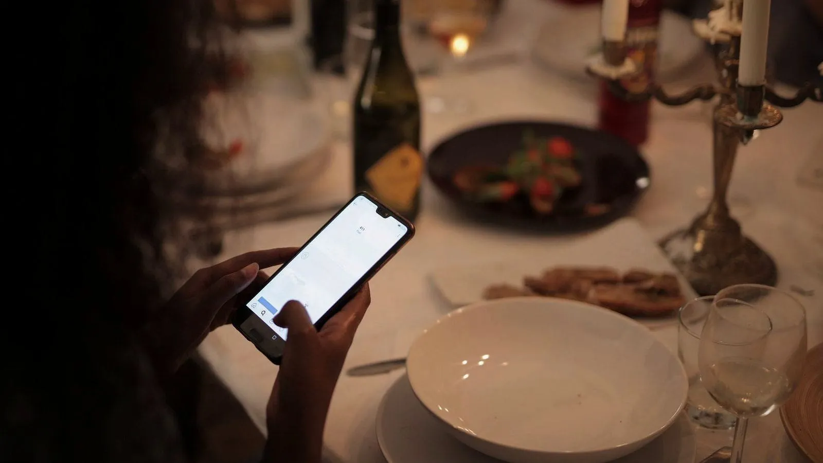 A diner checking her phone at a candle-lit table.