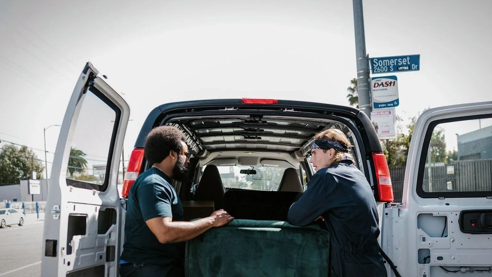 Two removal workers at the back of an open van in a city street.