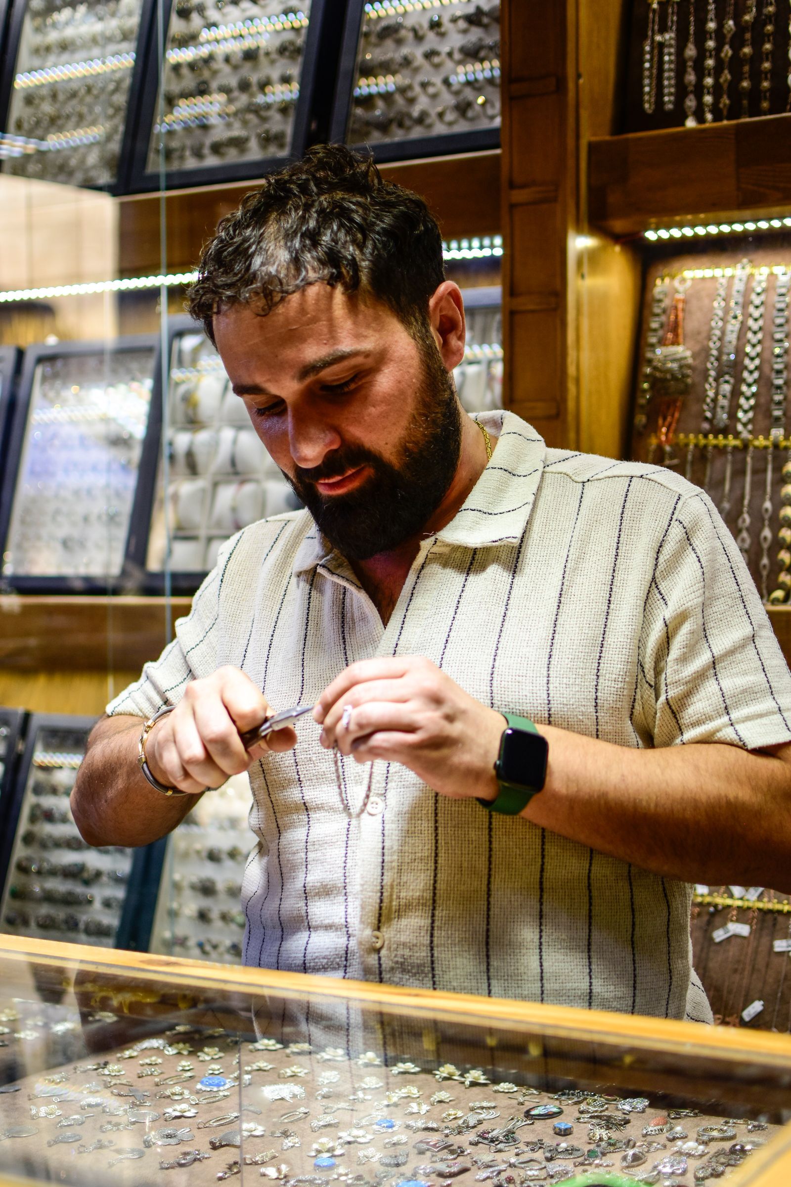 A jeweller at his shop counter, looking closely at a piece in his hands.