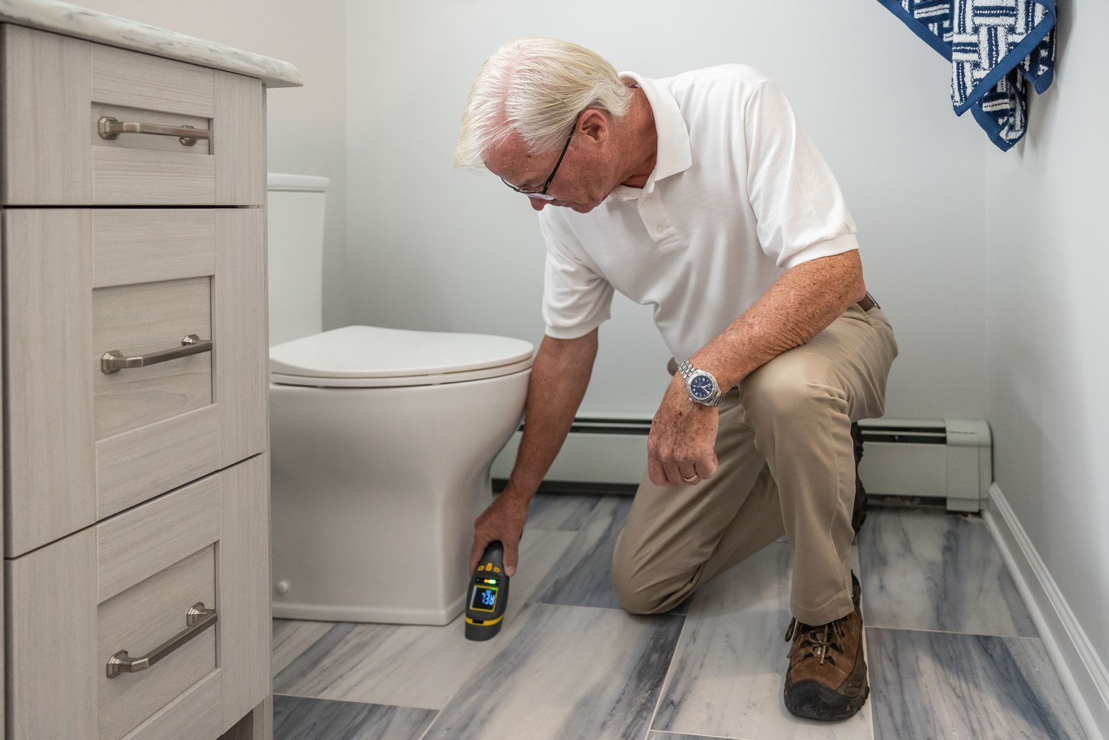 A plumber kneeling on a bathroom floor beside the toilet, checking the pipework.