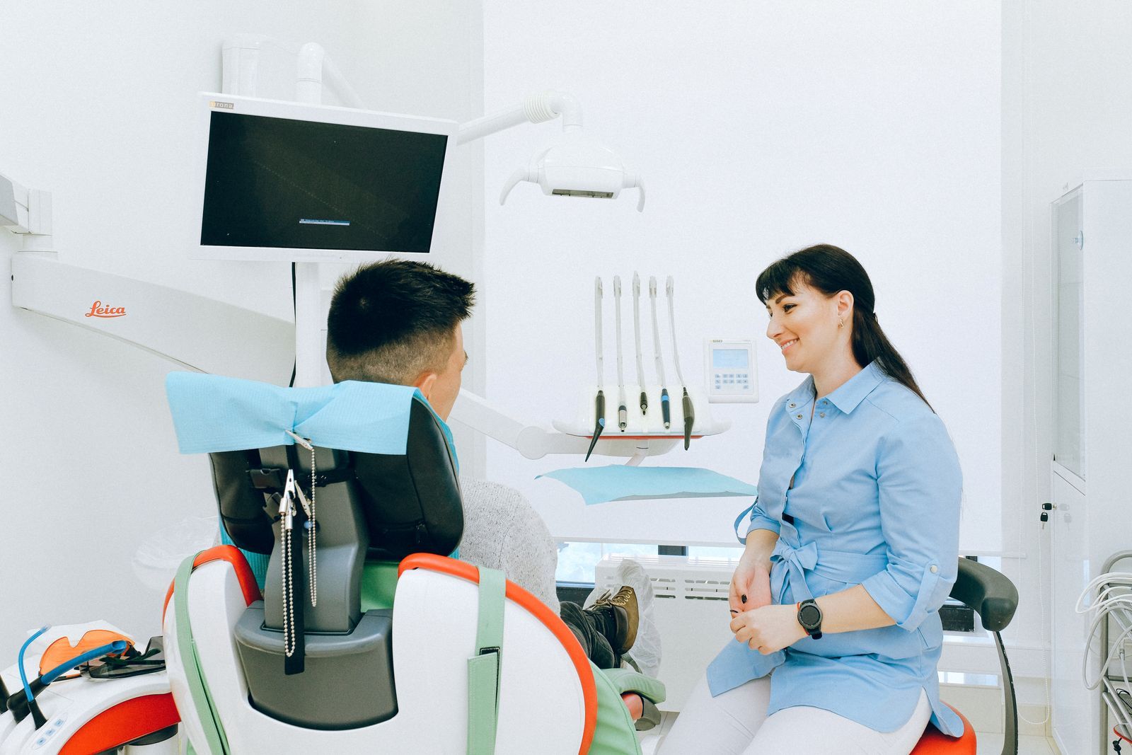 A dentist chatting with a smiling patient in the chair before a check-up.
