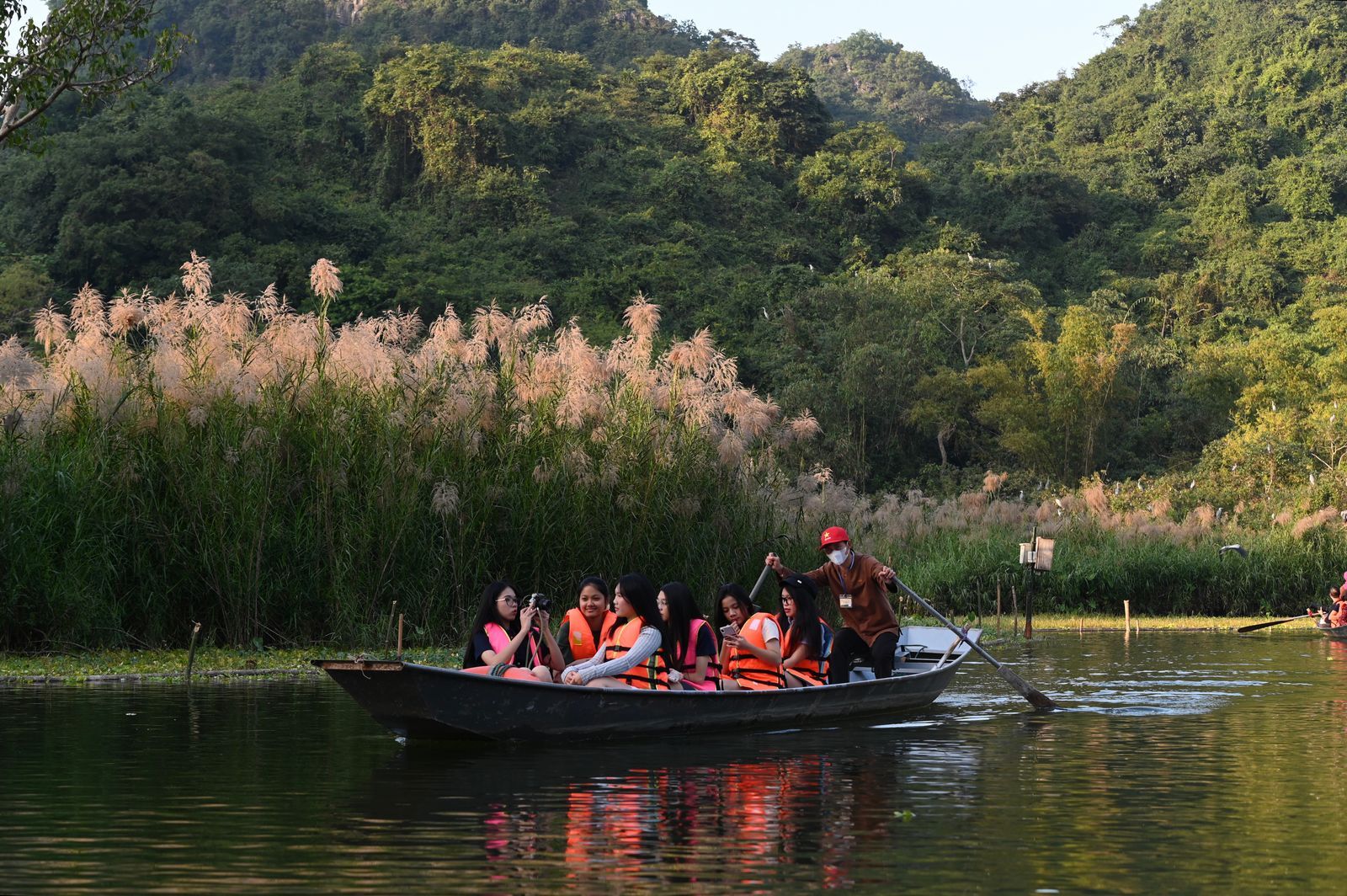 Visitors in life vests on a guided boat trip along a calm, green river.