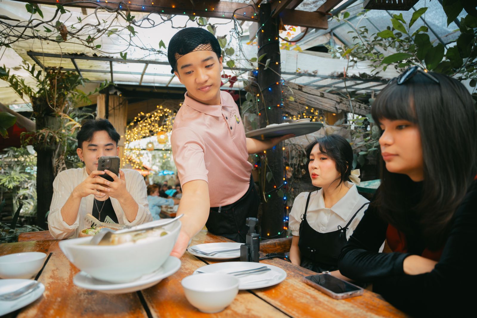 A waiter setting dishes down for a table of friends laughing over dinner.
