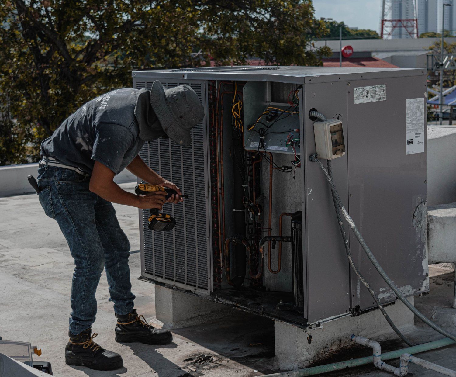 An HVAC technician servicing an air-conditioning condenser on a flat roof.