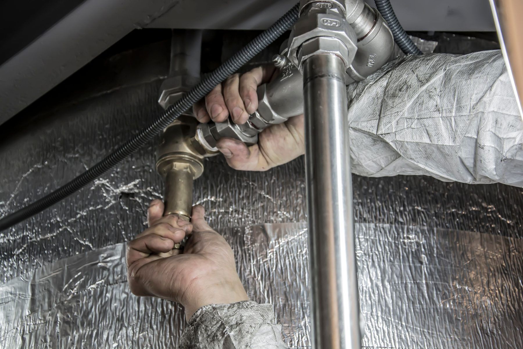 A plumber’s hands tightening a brass valve on the supply pipes.