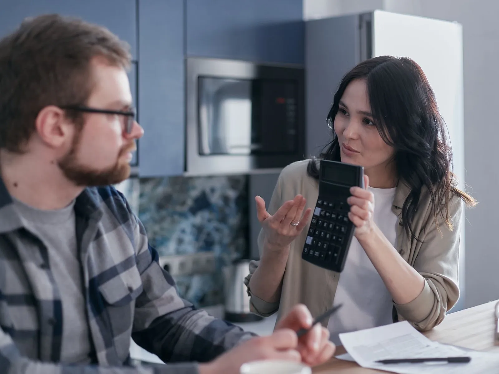 A couple at their kitchen table going over a price, one of them holding up a calculator.