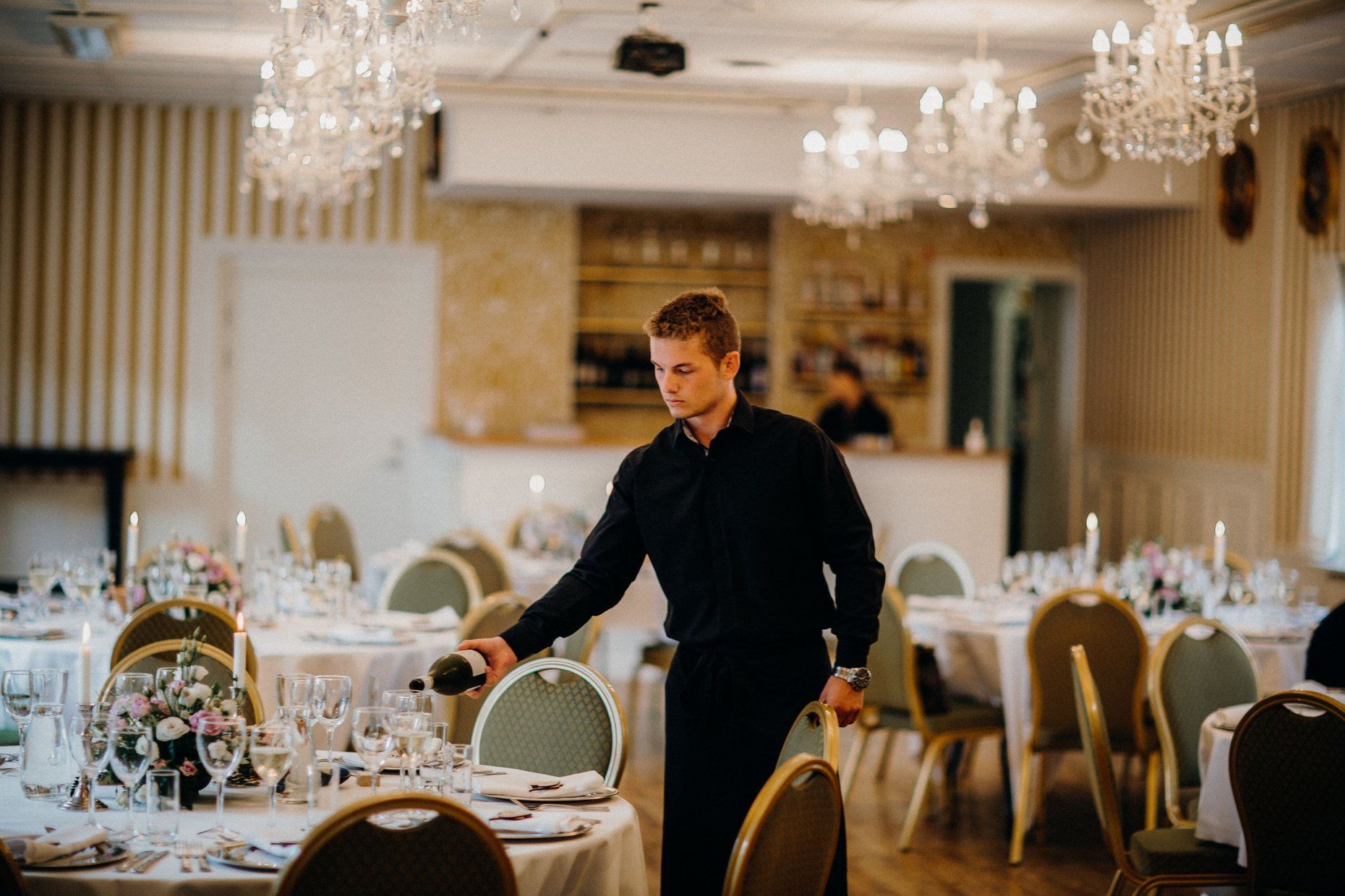 A waiter setting the tables of a chandelier-lit banquet hall before an event.