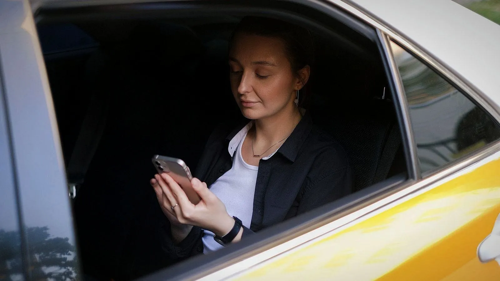 A passenger in the back of a yellow cab, reading something on her phone.