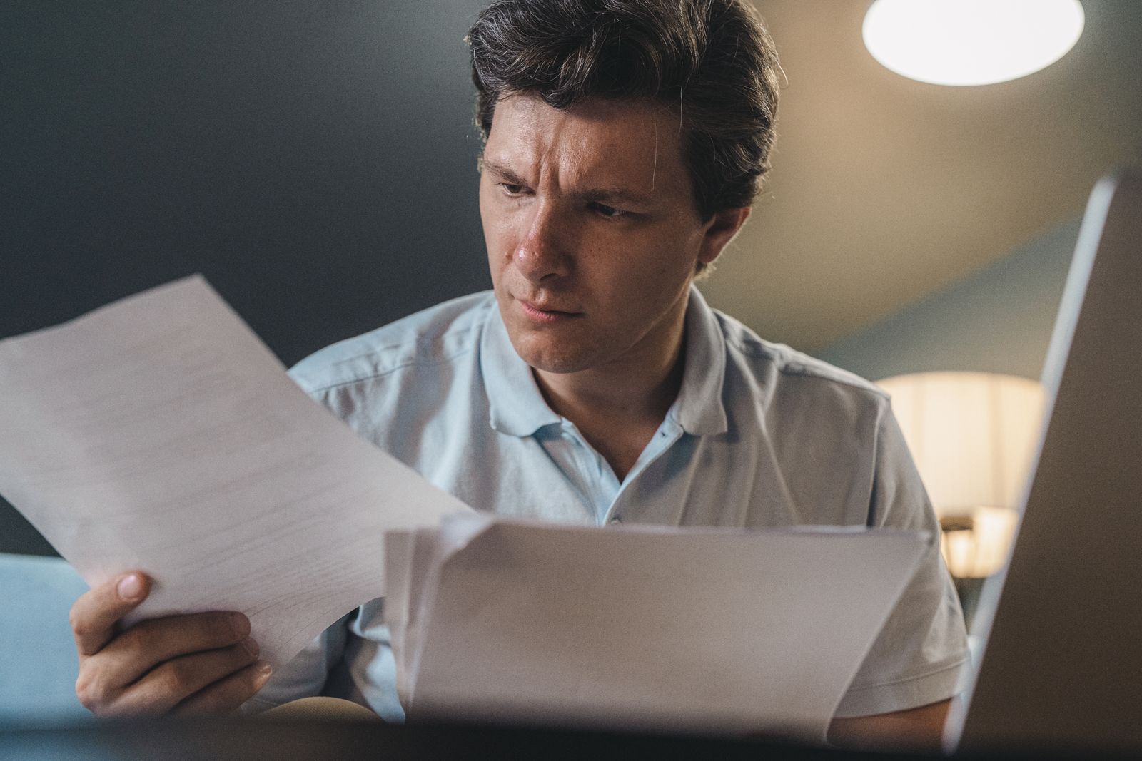A man reading a printed page closely at his desk, checking it line by line before he decides.