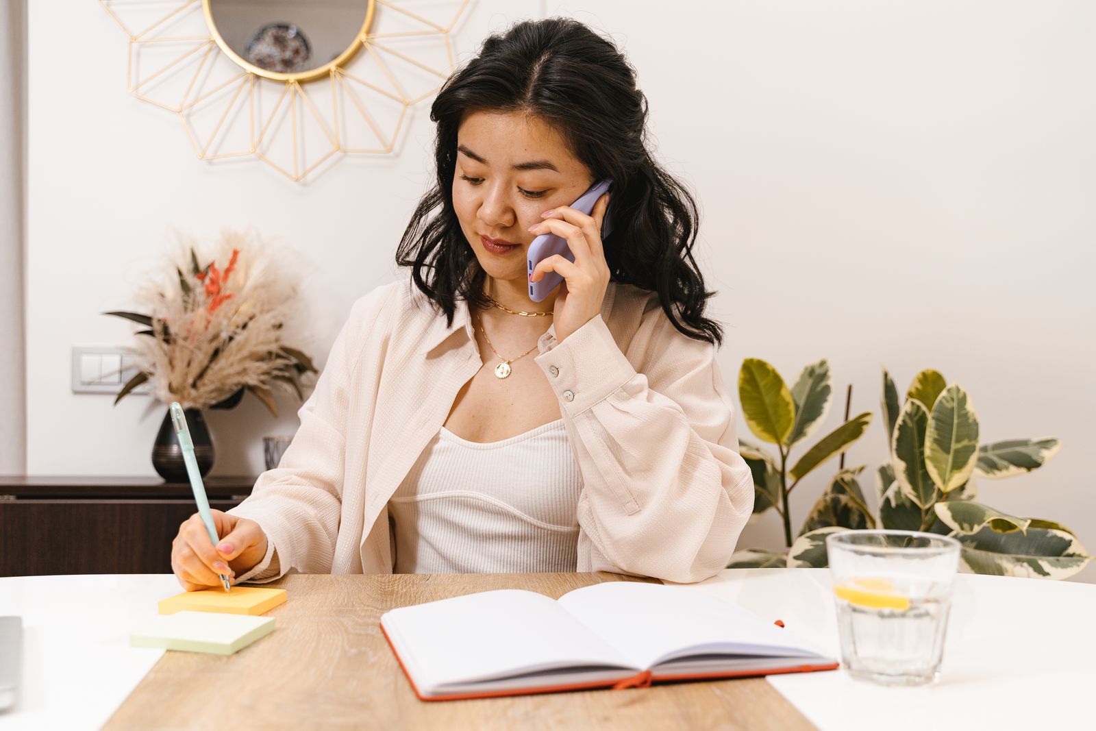 A business owner on a phone call at her desk, writing notes as she listens.