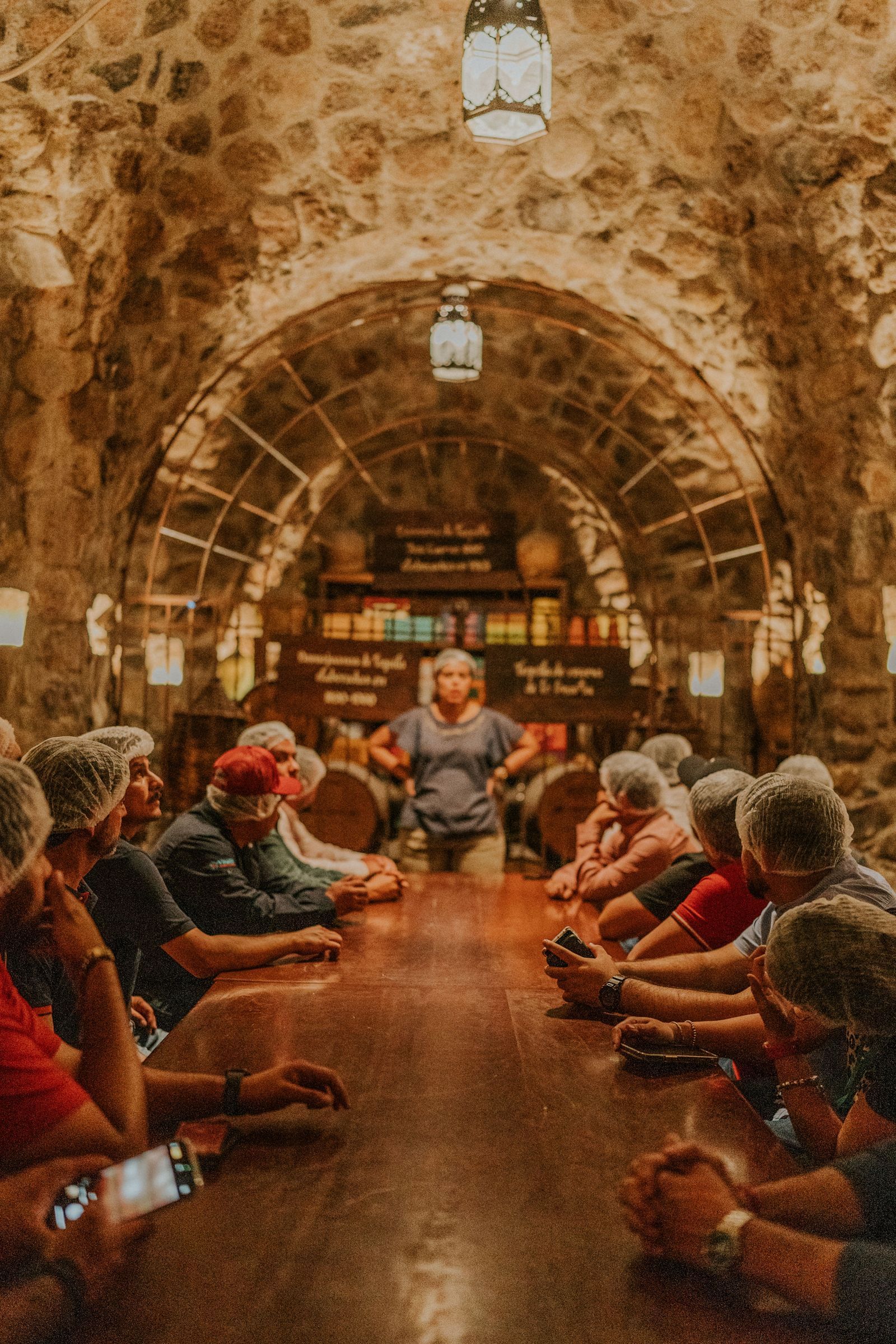 A tour group sitting in a stone wine cellar, listening to the guide.