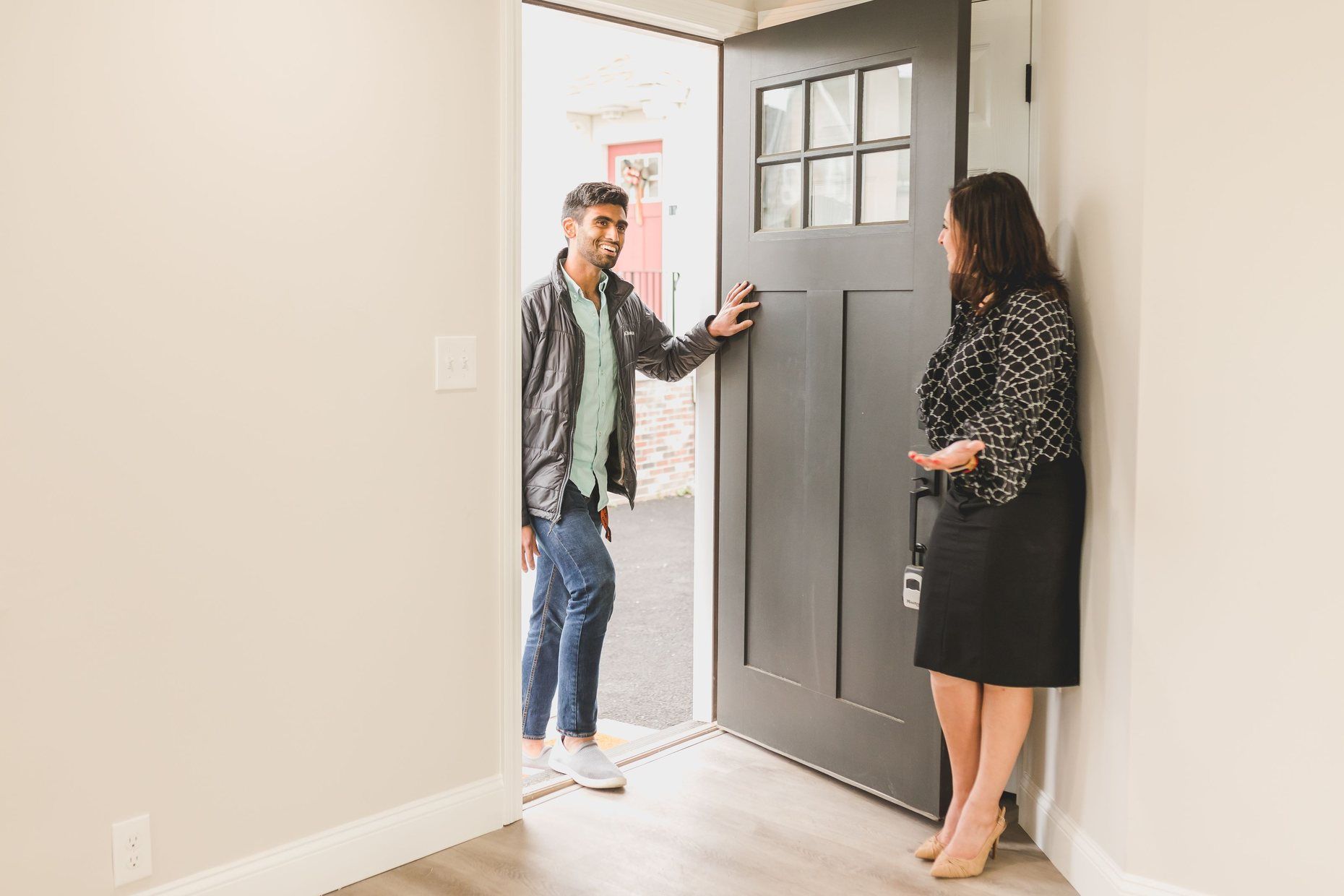A real estate agent opening the front door of a home to a smiling buyer.