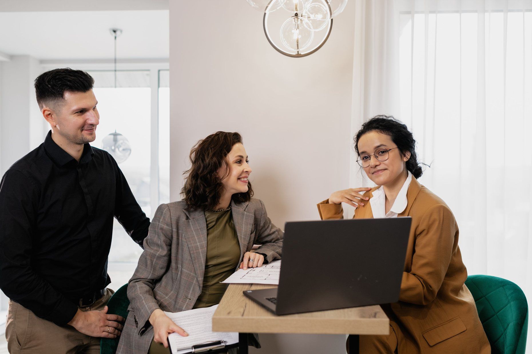 Two agents and a client going over a listing on a laptop in a bright real estate office.