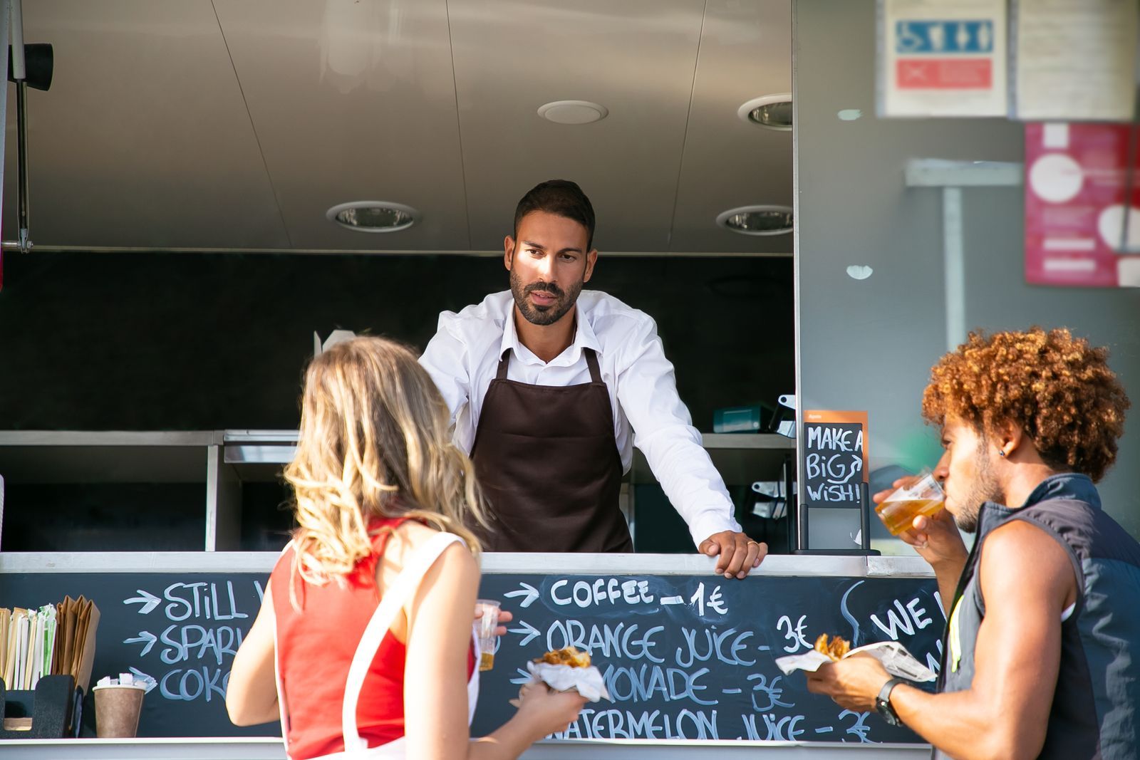 A food truck owner chatting with two customers at the serving hatch.