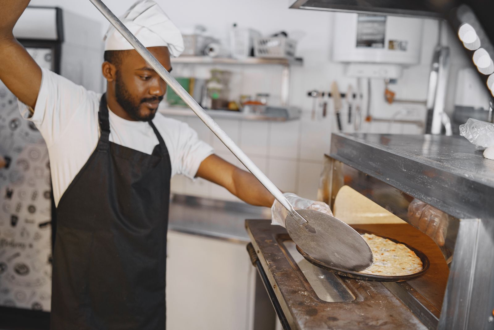 A pizza maker sliding a pizza into the oven with a long peel.