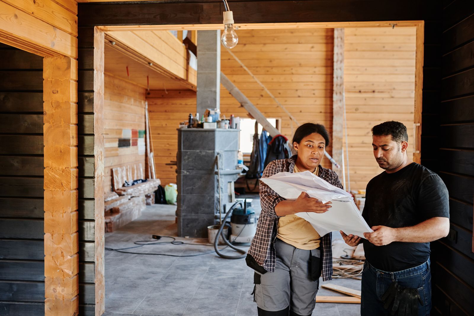 Two builders going over a plan together inside a house under construction.