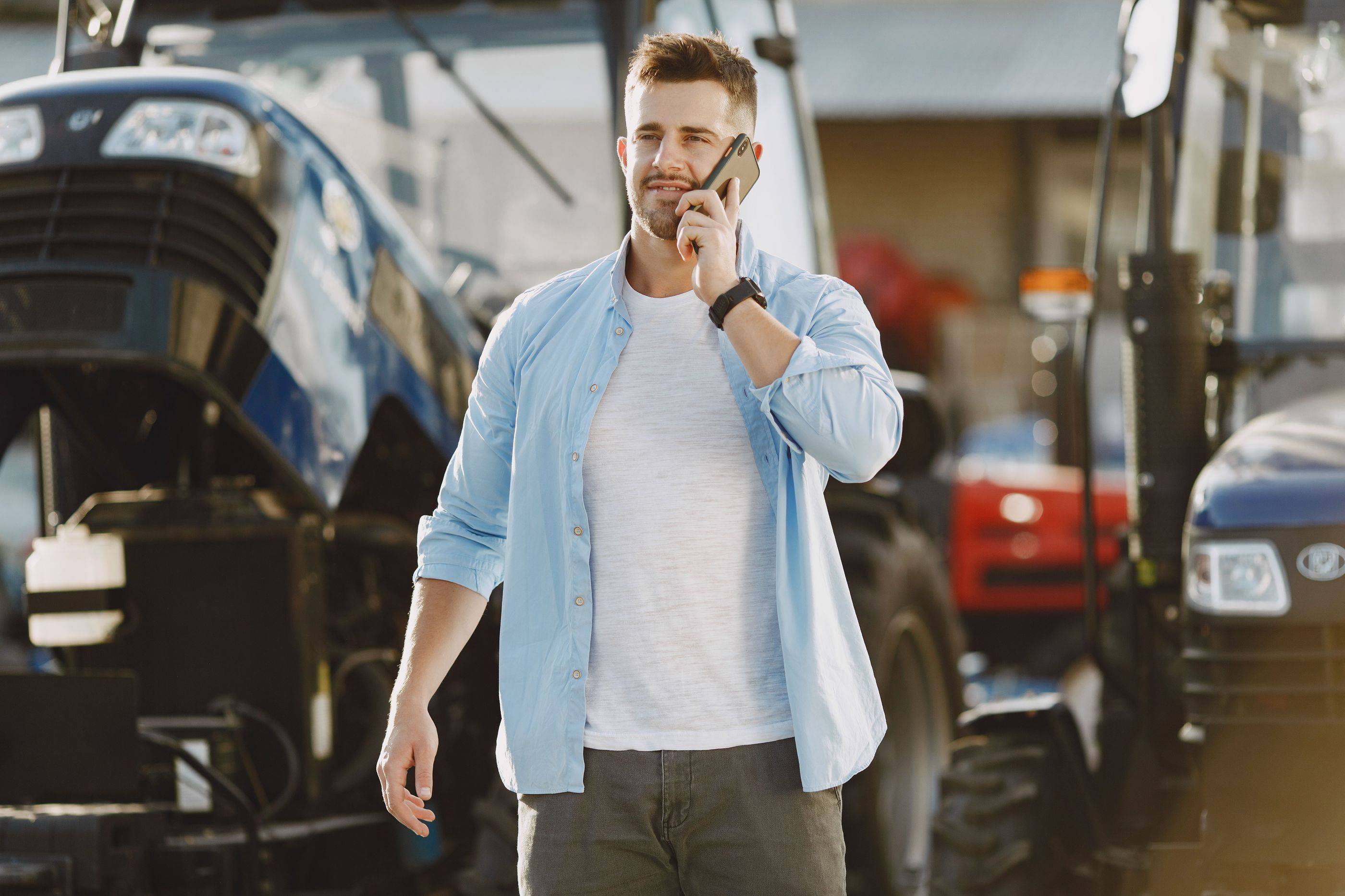 A farm machinery dealer takes a customer’s call as he walks across his yard between the tractors