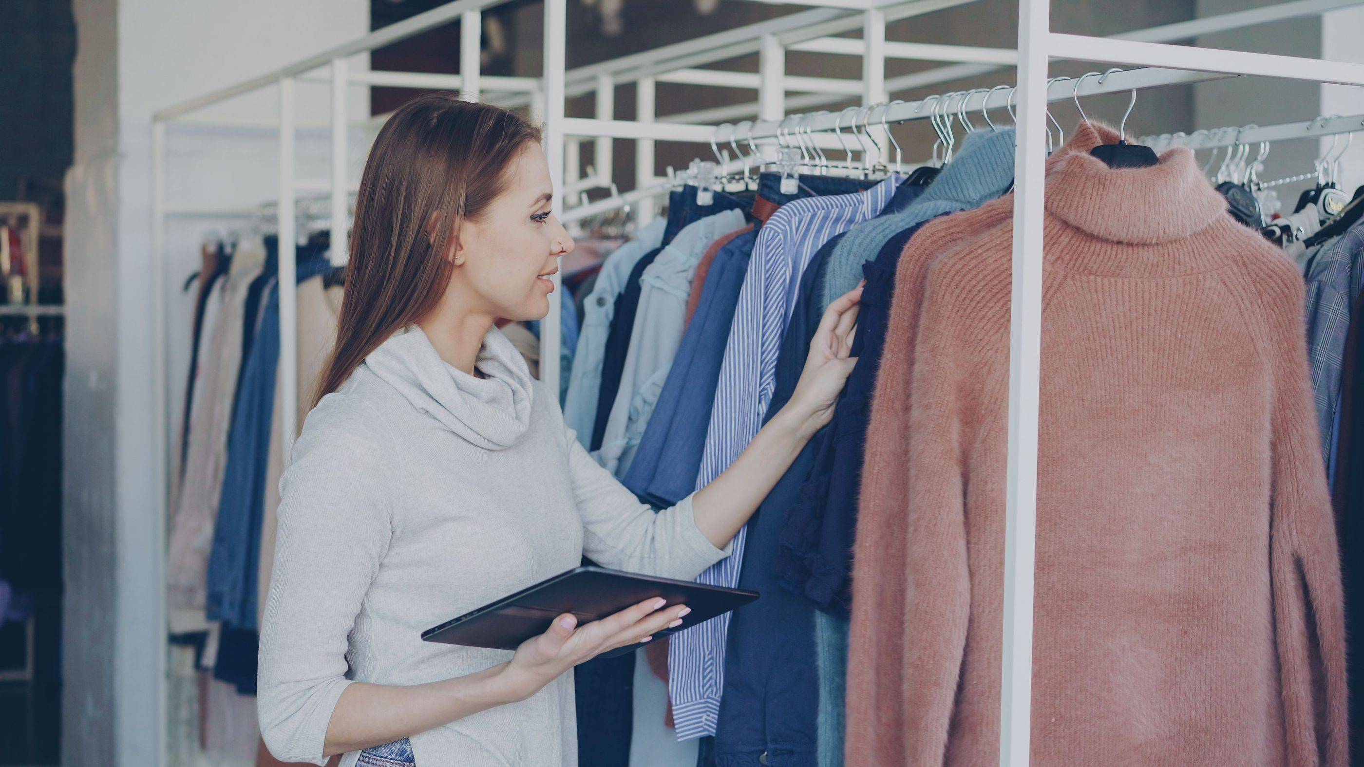 A boutique owner checks her tablet beside the clothing rail while the shop carries on