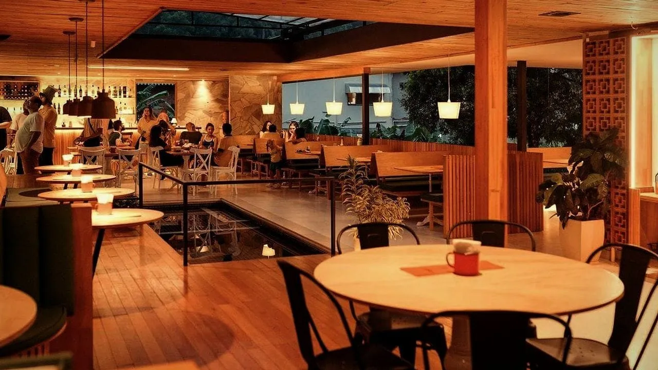 A warmly lit restaurant dining room with tables set and guests at the bar.