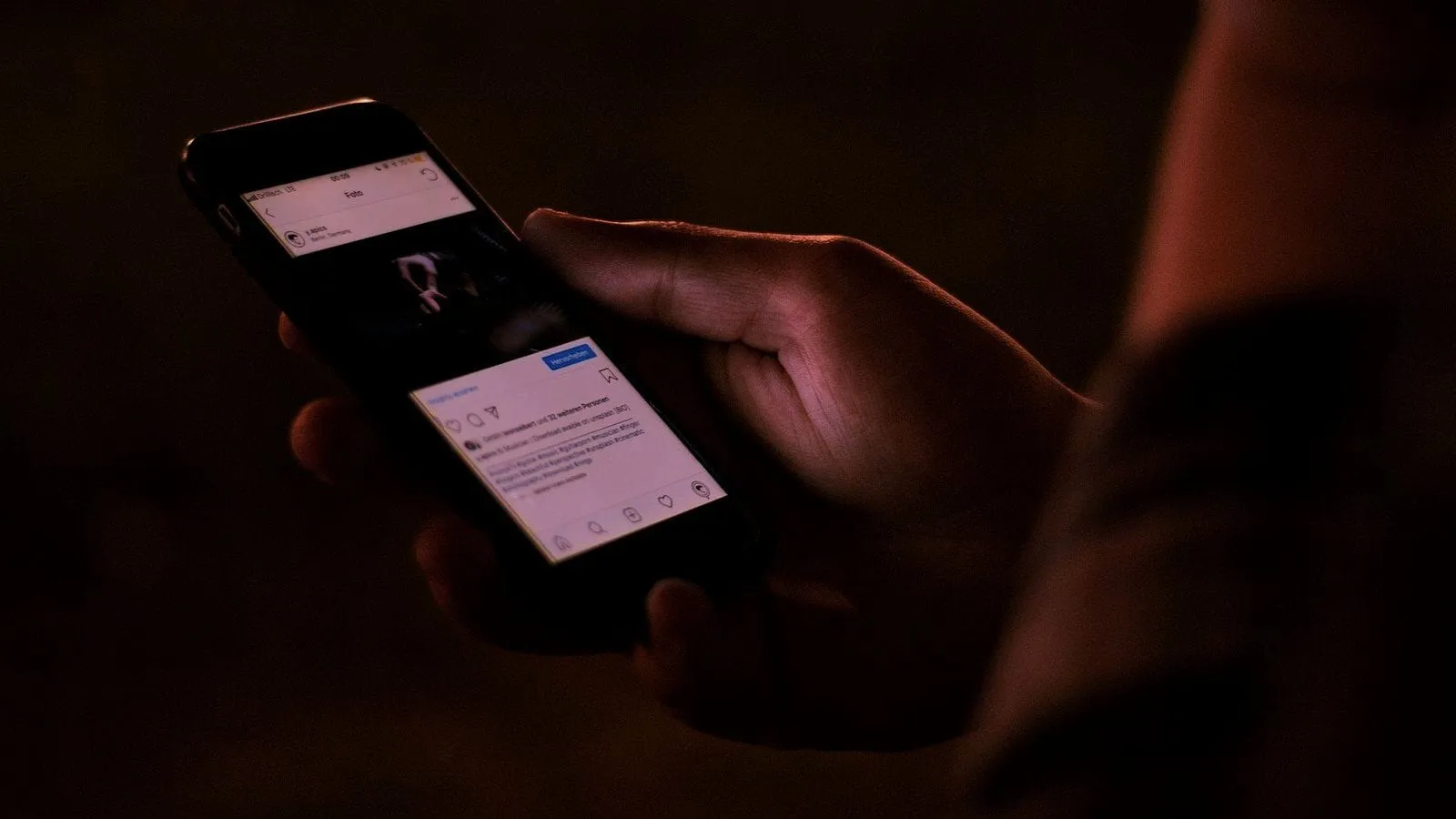Close-up of a hand holding a phone in a dim room, a post open on the screen.