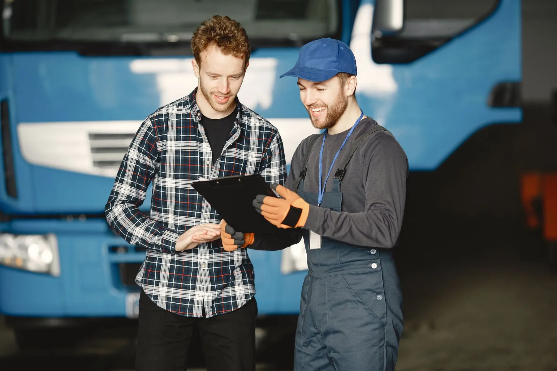 A mechanic in a cap smiling as he goes over a job sheet with a customer in his workshop.