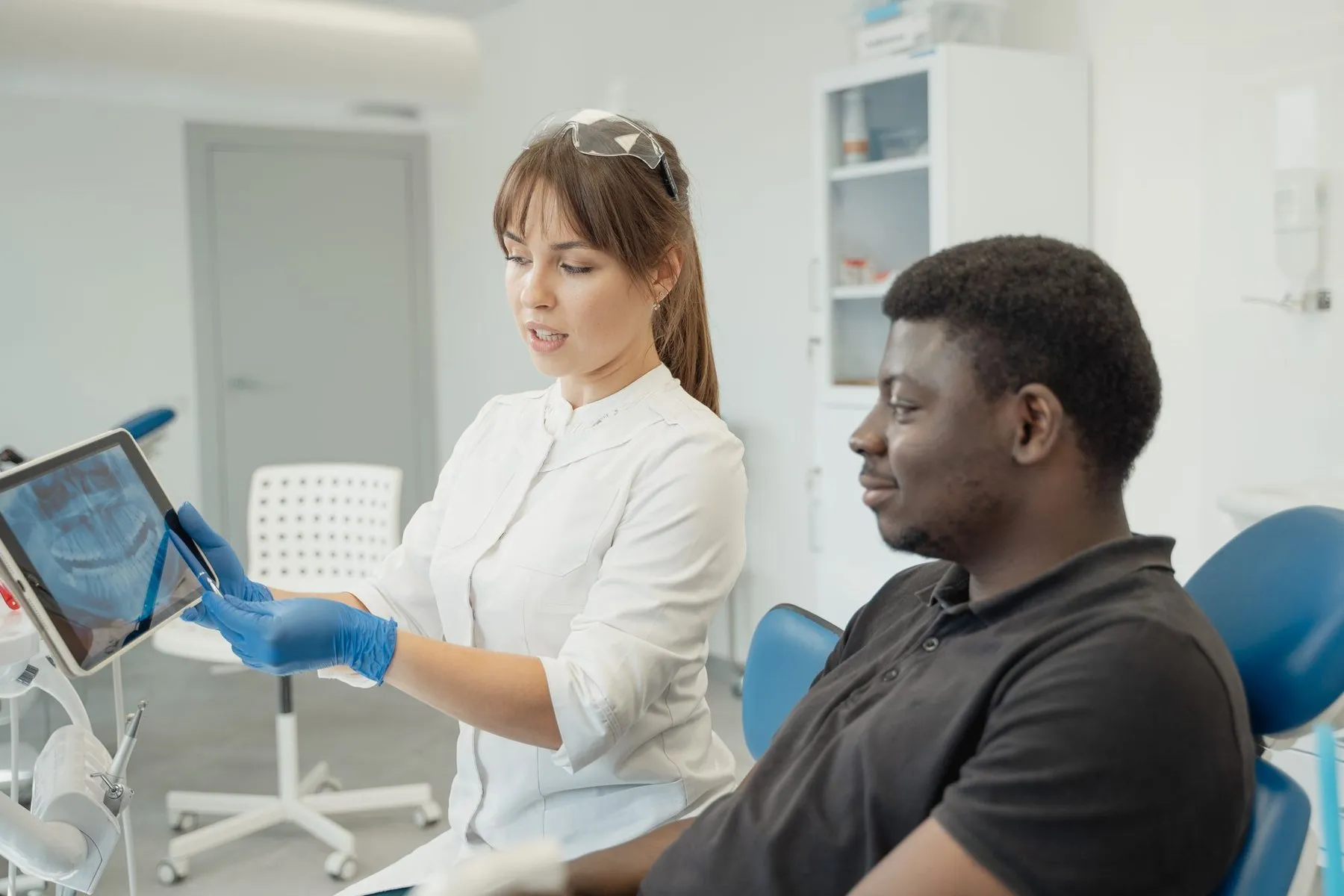 A dentist showing a smiling patient in the treatment chair his X-ray on a tablet.
