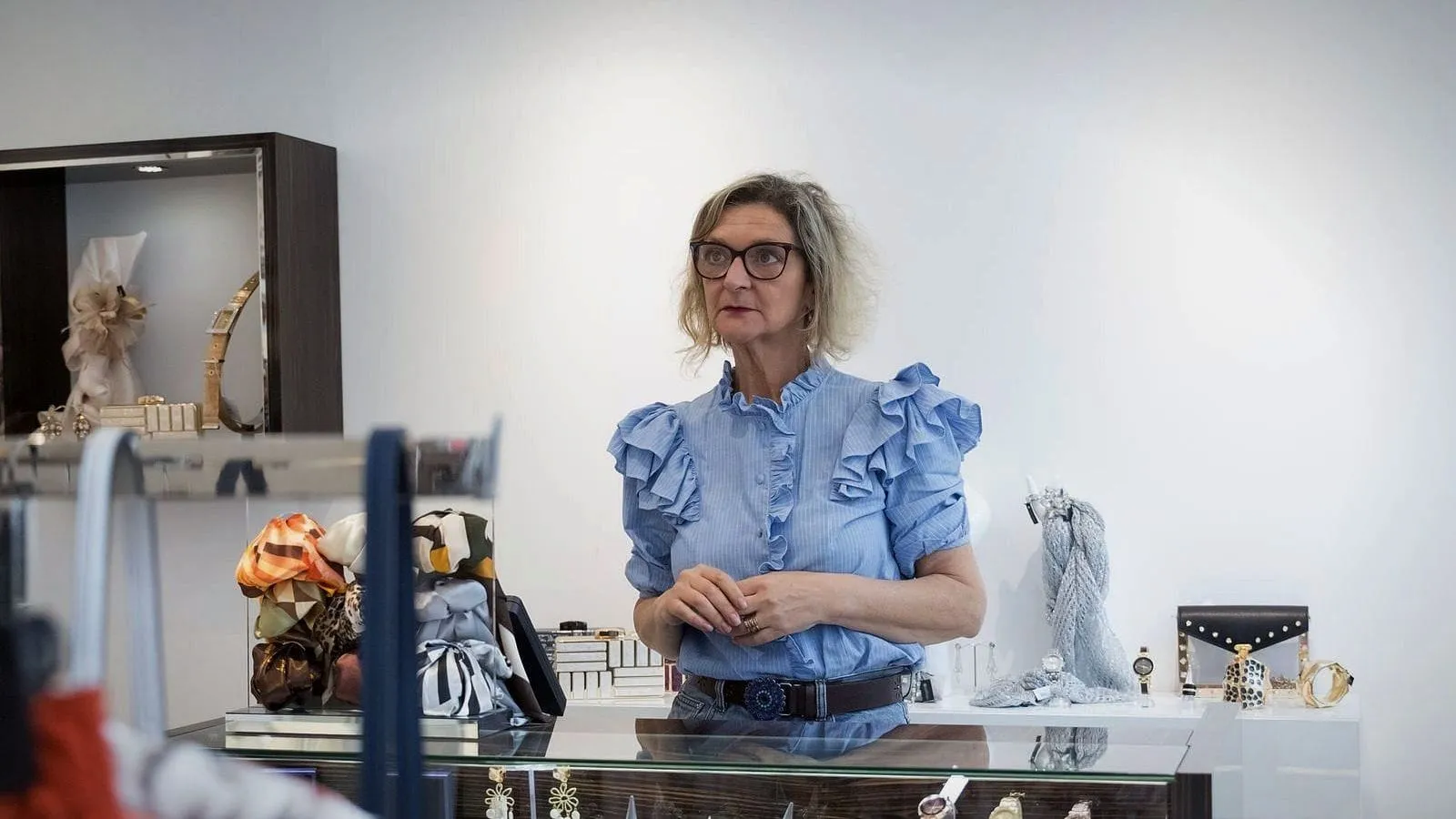 A shop owner in a blue blouse standing behind the counter of her bright boutique.