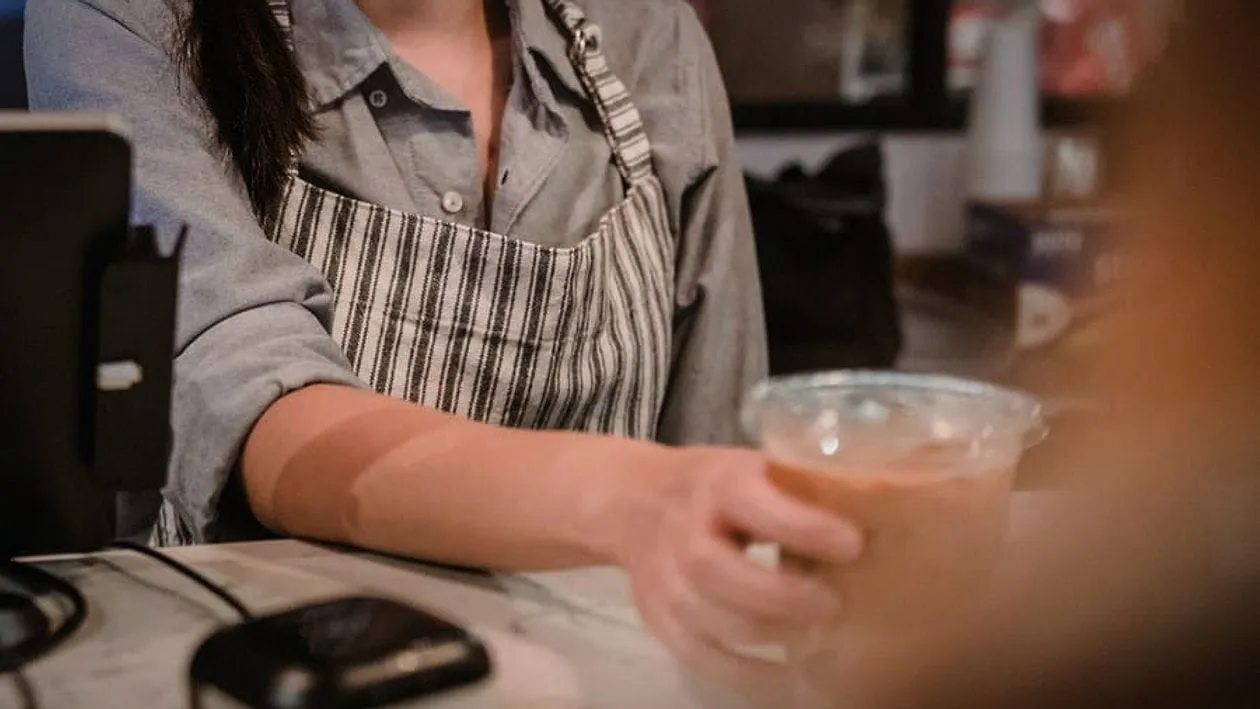 A barista in an apron handing a drink across the counter.
