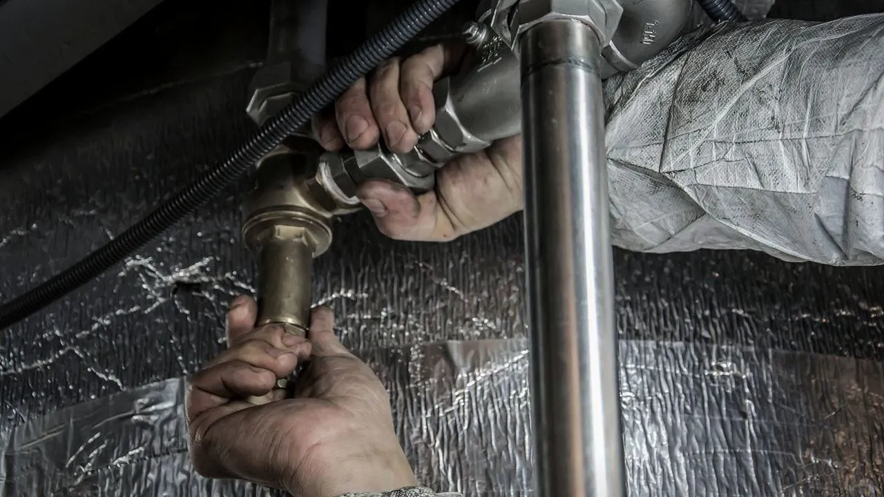 Hands tightening a pipe fitting under a sink.