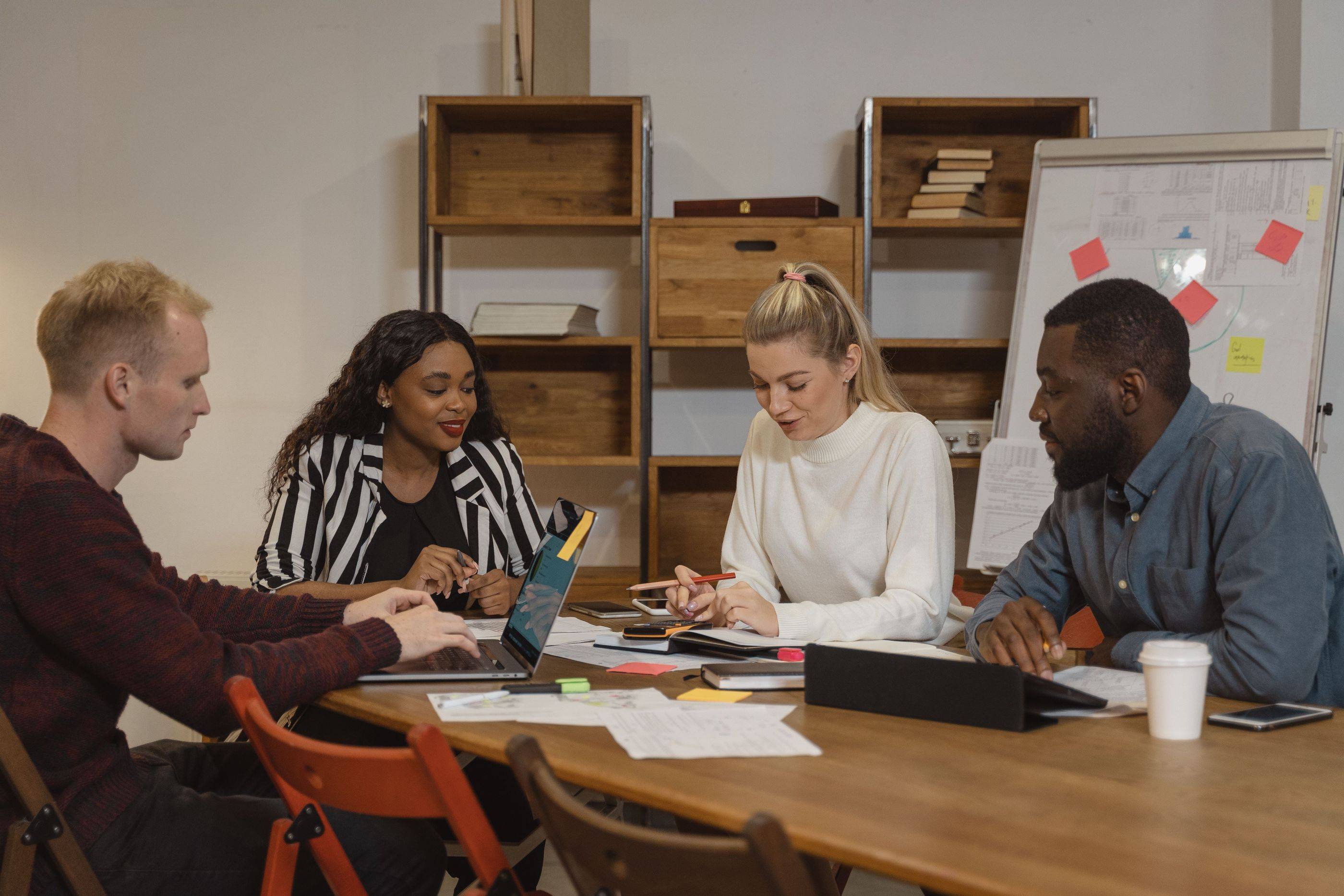 A team of four works through notes and papers together at a long table