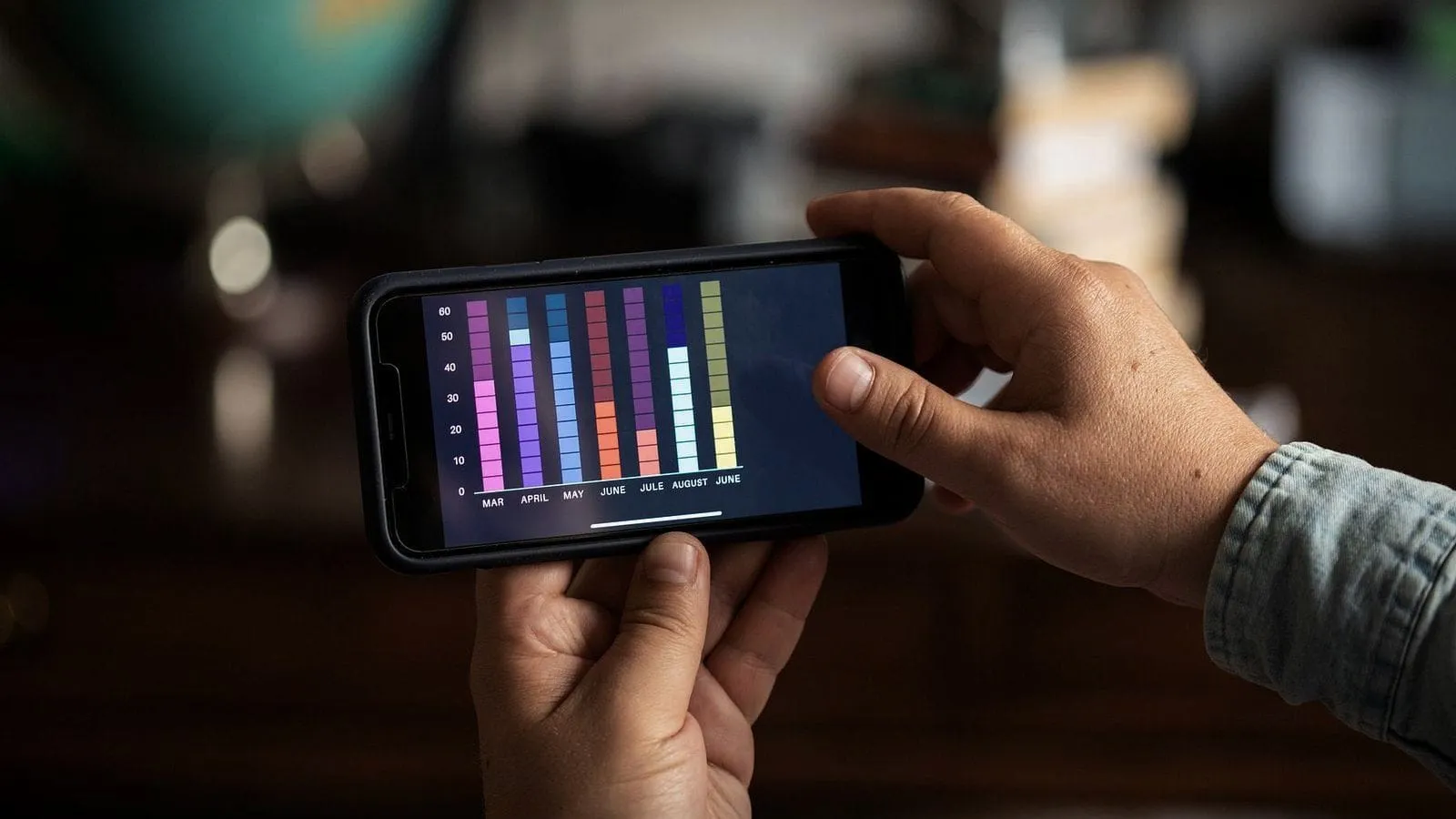 Two hands holding a phone sideways, its screen showing a colourful bar chart.